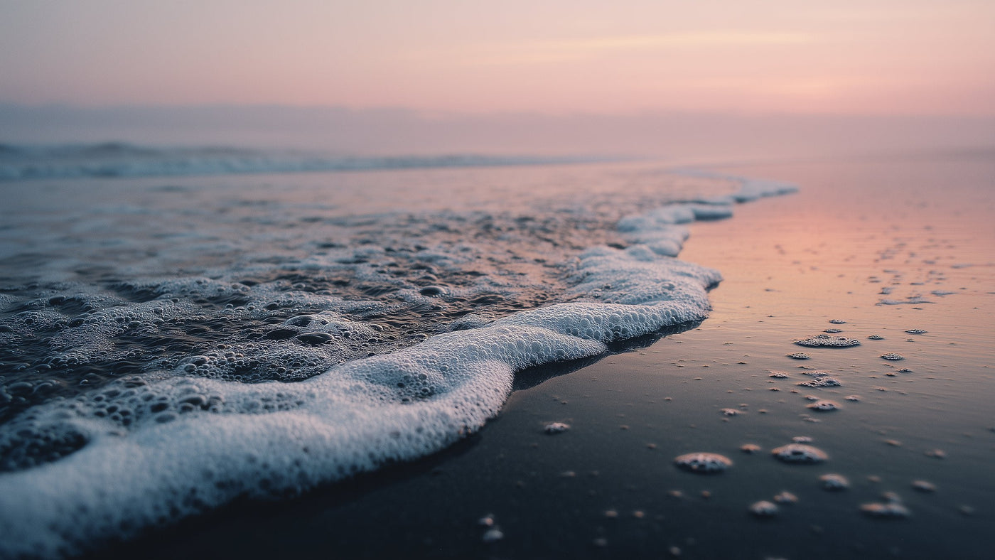 Sea foam sweeping across dark volcanic sand at dawn
