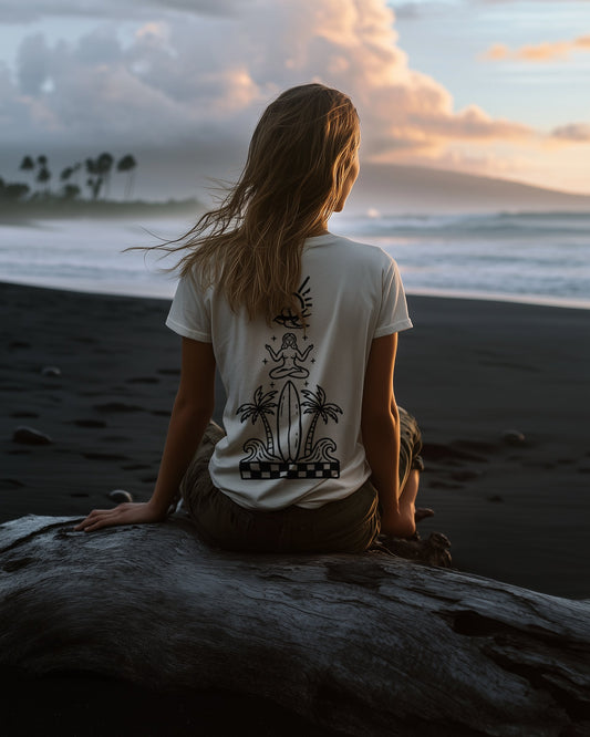 Back of the Tarot tee — woman seated on driftwood on a black-sand beach at dusk, the tarot mark printed in black